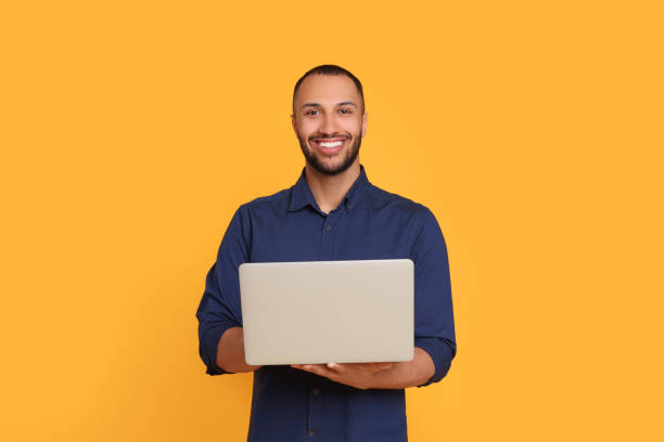 istock Smiling young man working with laptop on yellow background 1678874913