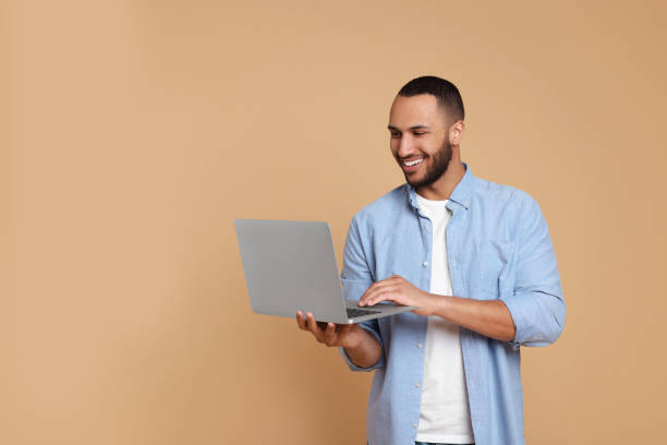 istock Smiling young man with laptop working on beige background, space for text 1678874920