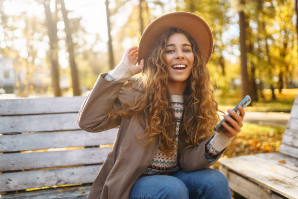 istock Cute lady in a hat and coat holds a smartphone. 1678878022