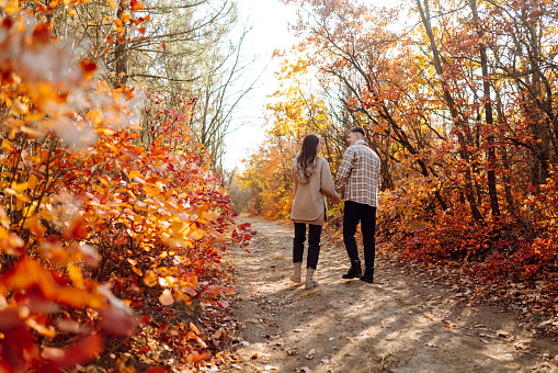 Young man and woman are walking, spending time together in the autumn forest. Beautiful couple enjoying nature outdoors in autumn. Concept for style, fashion, love or relaxation.