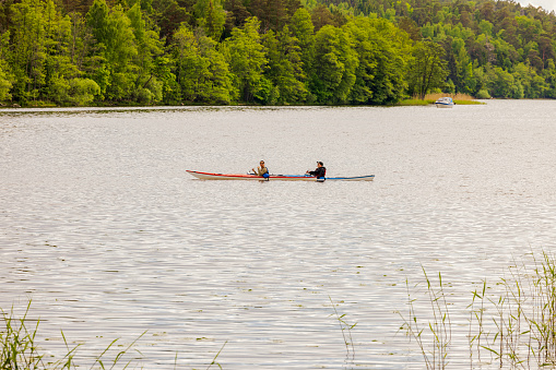 09.13.2023. Sweden, Europe. Uppsala.  View of two man in canoe on lake on green trees coastline background. Sweden, Europe.