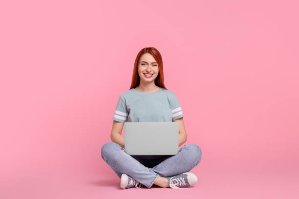 istock Smiling young woman working with laptop on pink background 1678893889