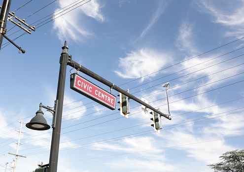 A red and white Civic Centre sign hangs with a traffic light and street lamp in a downtown district. Summer morning with light clouds over Metro Vancouver, British Columbia.