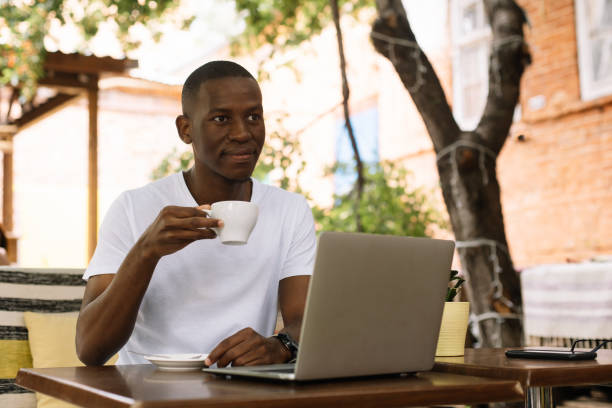 istock Confident and smiling multiracial businessman drinking coffee, working online using laptop in outdoor cafe. Remote job 1678995089
