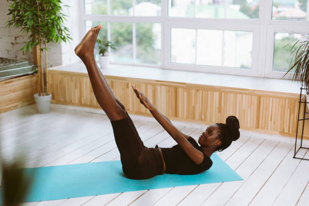 istock Athletic afro american woman lying on back and doing fold exercise with outstretched legs and arms on gym mat in photo studio. Sports course, exercise technique, pumping up press, beautiful figure 1679002474
