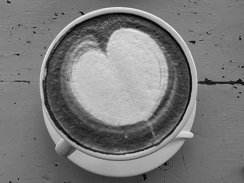 A cup of coffee with heart pattern in a white cup on wooden background. Black and white photo.