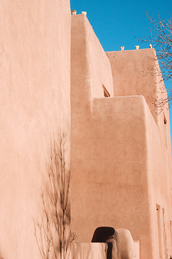 Vertical closeup photo of the exterior facade and rooftop of an adobe building on a sunny day in Winter. Santa Fe, New Mexico.