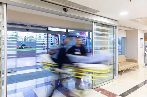 The paramedics take the patient from the ambulance to the hospital on a stretcher. Two paramedics and a patient. Modern ambulance. Emergency room entrance of a large hospital.
