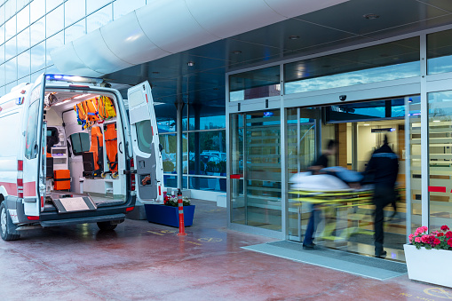 The paramedics take the patient from the ambulance to the hospital on a stretcher. Two paramedics and a patient. Modern ambulance. Emergency room entrance of a large hospital.