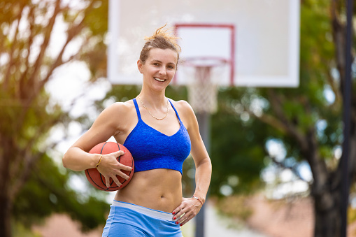 A middle aged woman playing basketball at the park.