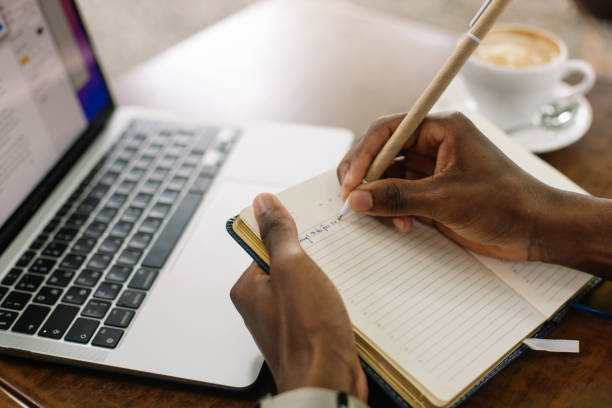 istock cropped multiracial businessman using laptop, taking notes in workbook, drink coffee in street cafe. High angle 1679148417