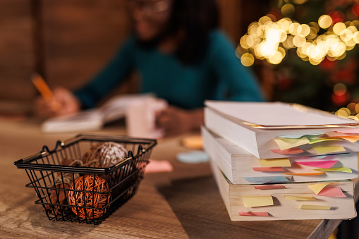 Selective focus shot of unrecognizable young woman sitting at home office desk, enjoying a hot beverage and writing her New Year's resolutions in a diary.