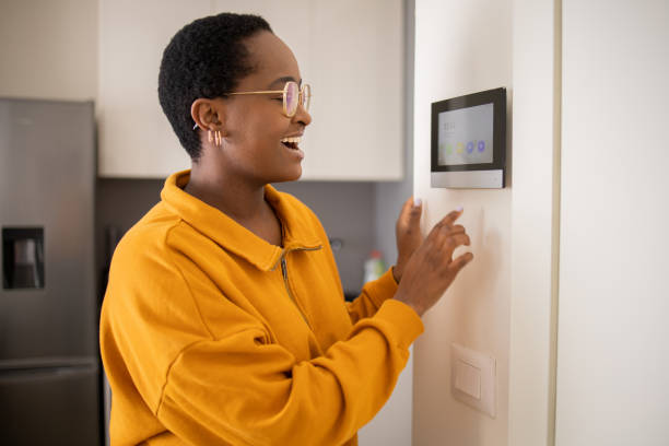 istock Young woman adjusts the temperature at home with a device on the wall 1679202418