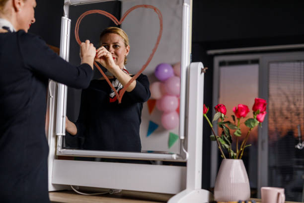 Happy woman standing in front of a mirror and drawing a heart with a red lipstick Portrait of happy mid adult woman smiling at her reflection in the mirror while drawing a heart with a red lipstick. mirror writing stock pictures, royalty-free photos & images
