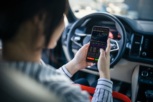 The convenience of investing in crypto in that you can do it anytime anywhere.Woman using smartphone to buy cryptocurrency in her car, blockchain investment, decentralize and Stock market concept.