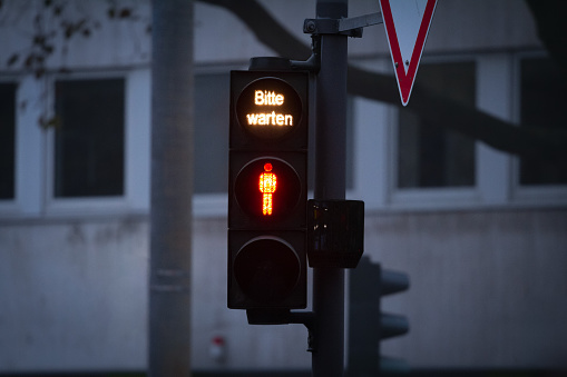 Selective blur on a German Pedestrian red light on a traffic light, abiding by the German and European traffic regulations, with the mention in German Bitte Warten meaning please wait at night.