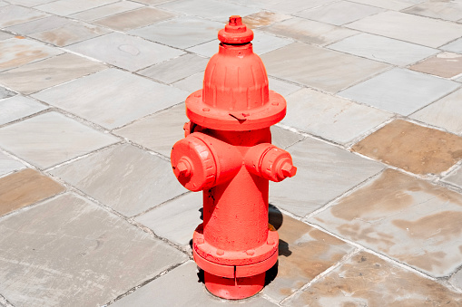 A bright red fire hydrant on a slate stone tile walkway on a sunny say.