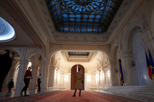 Picture of the interior of the Romanian palace of parliament, with a focus tourist taking pictures of a reception hall. The Palace of the Parliament, also known as the Republic's House or People's House/People's Palace, is the seat of the Parliament of Romania, located atop Dealul Spirii in Bucharest, the national capital. The Palace reaches a height of 84 m, has a floor area of 365,000 m² and a volume of 2,550,000 m³.
