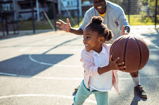 Close up of a Grandfather and granddaughter playing basketball together on an outdoors basketball court