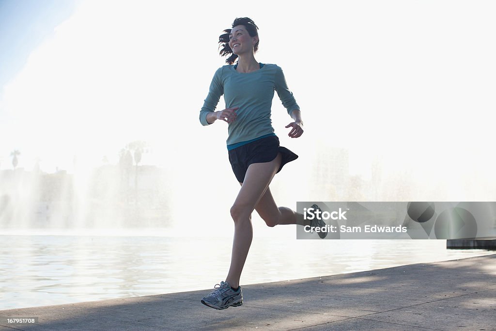 Donna che corre lungo il lago nel parco - Foto stock royalty-free di Correre