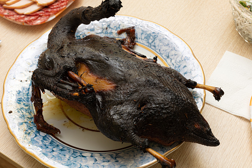 Burnt bird carcass on serving plate on dining table. Serve charred spoiled dish. Lousy housewife and bad chef. Overcook meat in oven. Terrible main course. Disgusting cooking, ruined celebration.