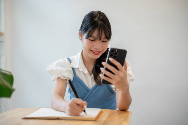 istock A woman making lists in her notebook while using her smartphone, sitting at a table indoors. 1679574572