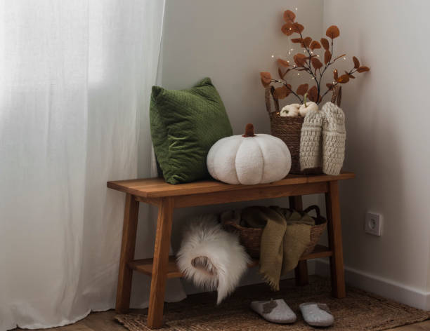 istock Cozy autumn interior - oak bench with a basket with blankets, pillows, branches, pumpkin, slippers in the living room interior 1679583074
