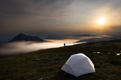 An adventure-seeking outdoorsman in front of a tent on a mysterious foggy mountainous terrain