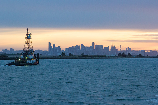 Tug boat leaving the Port of Oakland with the San Francisco skyline at setting sun.