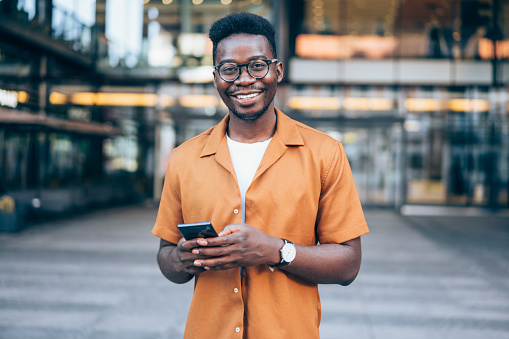 Shot of handsome african-american young man with smart phone texting outdoors in the city.