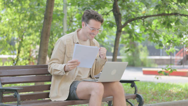 istock Modern Young Man Celebrating Contract while Working on Laptop Outdoor 1679665445