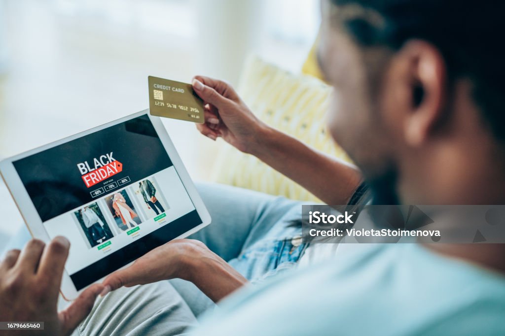 Couple shopping online on Black Friday. Close-up shot of a young couple holding a digital tablet and shopping online on Black Friday at home. Couple shopping online with credit card and digital tablet. Black Friday - Shopping Event Stock Photo