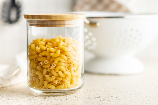 Raw macaroni pasta in glass bottle. Uncooked rigatoni in a glass jar.
