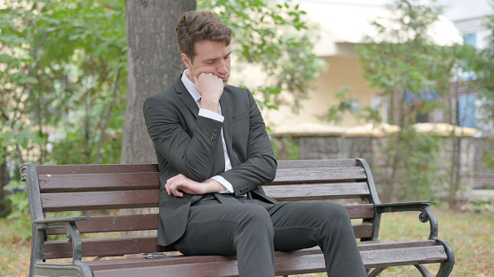 Tired Young Businessman Sleeping while Sitting Outdoor