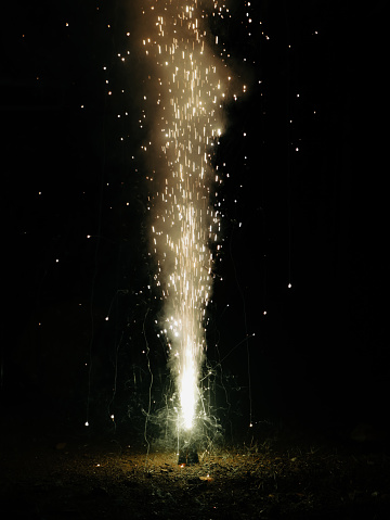 fountain of sparks and smoke bursting out of a diwali flower cone fire cracker at night during a festival