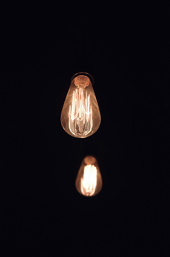 Low angle view of two retro Edison light bulbs against black background with copy space for greeting card or background - interior deco
