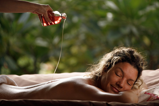 Unrecognizable massage therapist pouring oil on her customer's back before relaxing massage at the spa.