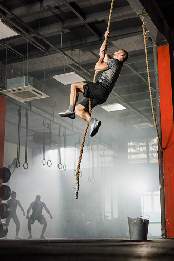 Young athletic man exercising strength on a rope in a gym.