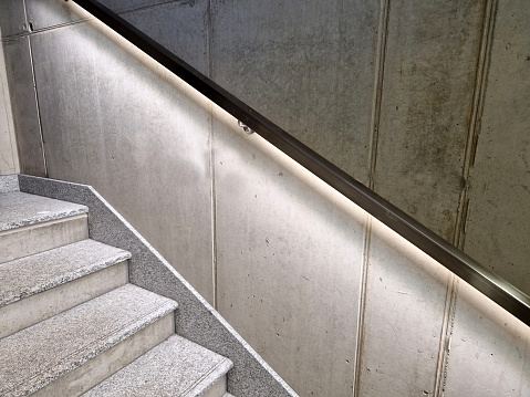 from the bottom of the handle is a recessed LED strip with yellow light. hidden built-in lamp shows a man's hand. the concrete side of the staircase with retaining walls  night, corridor, granite, included, under