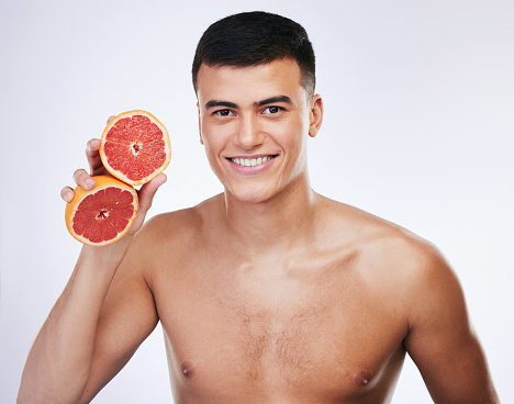 Skincare, grapefruit and smile with portrait of man in studio for beauty, detox and natural cosmetics. Vitamin c, nutrition and spa with person and fruit on white background for self care and glow