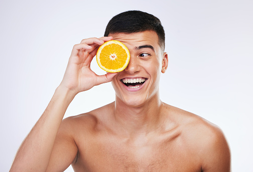 Beauty, orange and happy with face of man in studio for health, detox and natural cosmetics. Vitamin c, nutrition and summer with face of person and fruit on white background for self care and glow