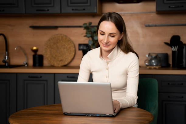 istock A brunette woman uses a laptop while sitting in the kitchen 1679828660