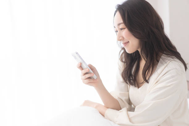 istock A woman is sitting on her bed and using her cell phone. 1679840734