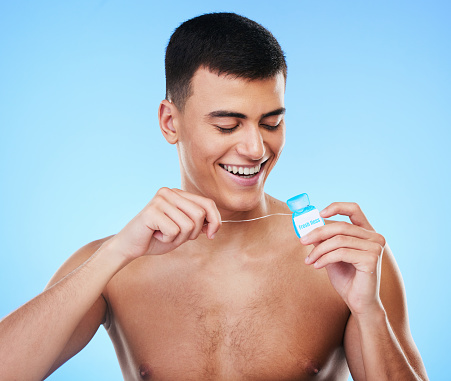 Dental floss, man and teeth cleaning for healthcare, wellness and morning care in studio. Blue background, male model and happy from mouth hygiene with smile from healthy product for tooth protection