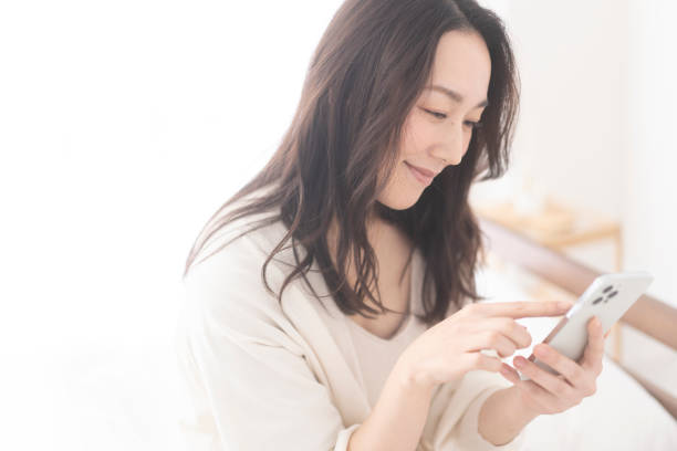 istock A woman is sitting on her bed and using her cell phone. 1679841827