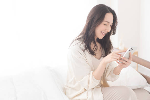 istock A woman is sitting on her bed and using her cell phone. 1679841844
