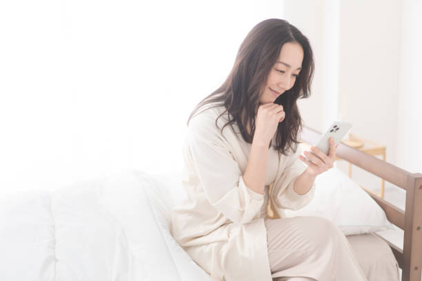 istock A woman is sitting on her bed and using her cell phone. 1679841850