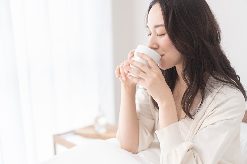 A young Japanese woman is holding a white cup and drinking a drink.