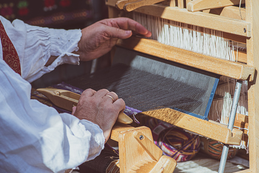 A craftswoman working on an ancient wooden weaving loom in traditional dress in an arts and crafts fair in Vilnius, Lithuania