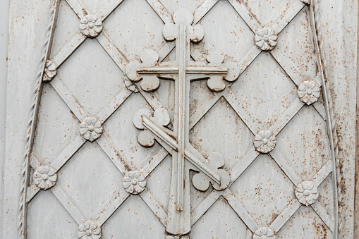 Old metal gray rust door. Detail of metal door with traditional christian ornament. Iron door of the church or cathedral decorates with floral ornaments and christian cross
